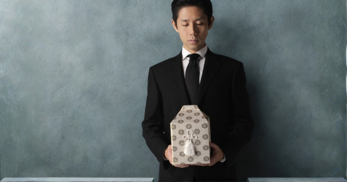 喪主の男性が骨壺を抱えて故人を偲ぶイメージ